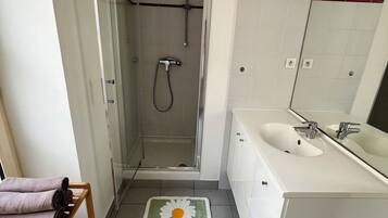 Een badkamer met een douche, een wastafel en een houten plank met handdoeken.