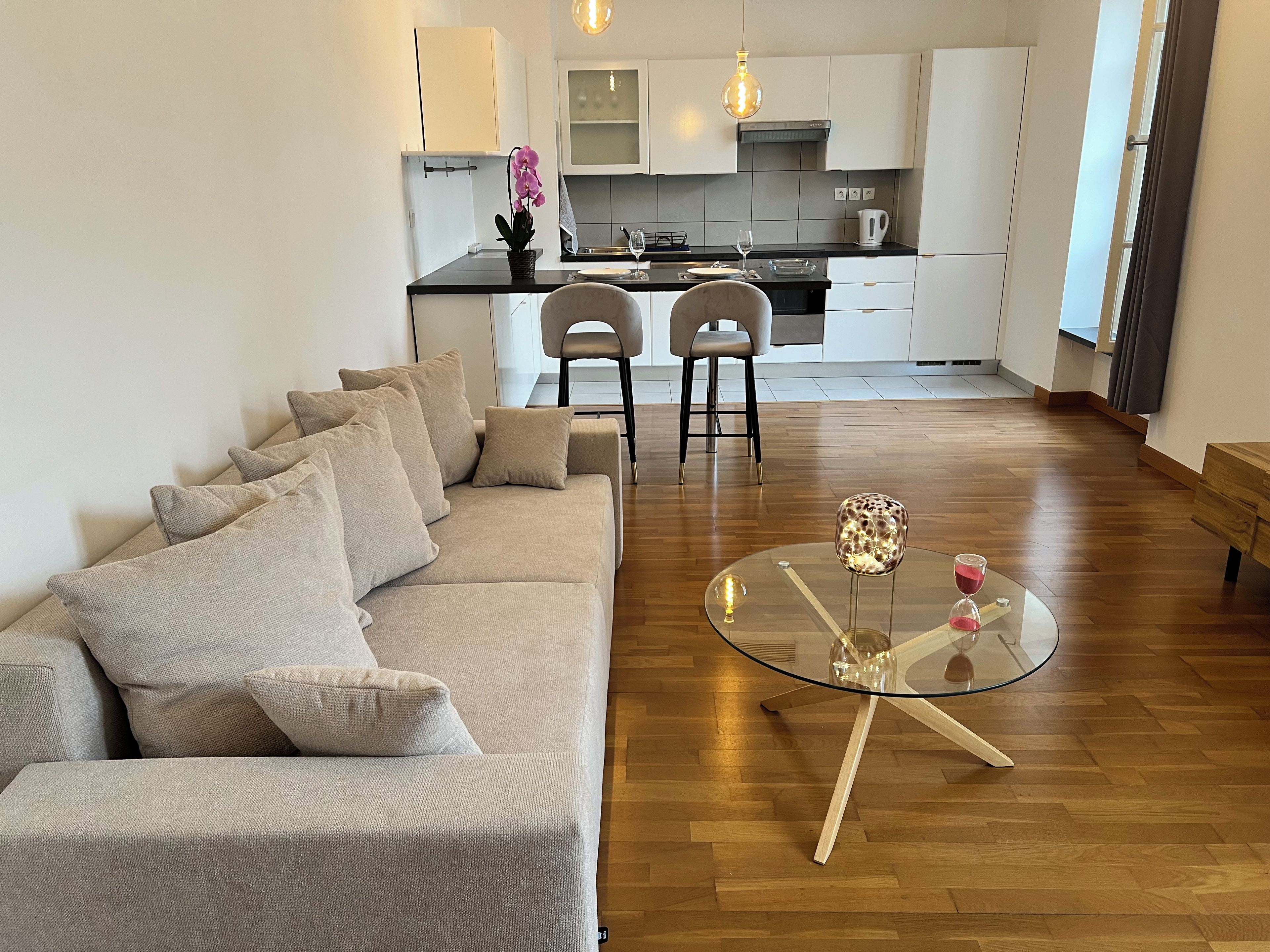 A modern living room with a sofa, a glass coffee table, and a kitchen in the background.