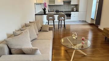 A modern living room with a sofa, a glass coffee table, and a kitchen in the background.