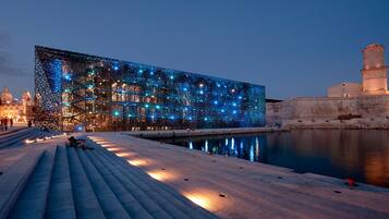 Een waterkantpromenade met een modern gebouw versierd met blauwe lichten, een rustig wateroppervlak en een historische toren.