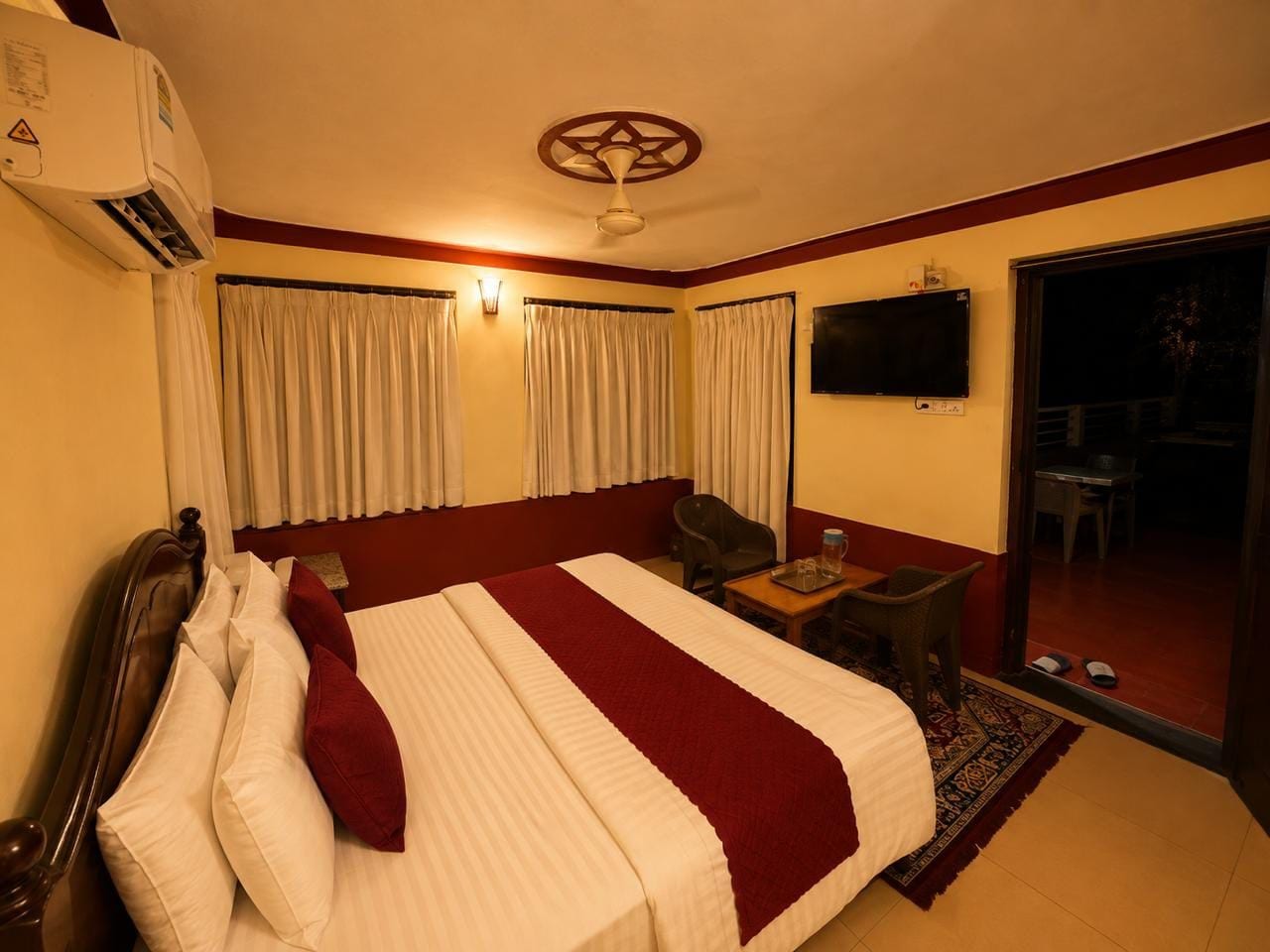 A hotel room with a bed, a desk, a chair, an air conditioning unit, and a television.