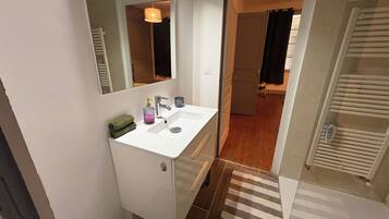 Een badkamer met een witte wastafel, een spiegel, een handdoekhouder en een douche.