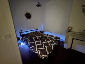 Une chambre à coucher avec un lit, une table de chevet, un ventilateur fixé au mur et une cheminée.