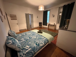 Ein Schlafzimmer mit einem Bett, einem Schreibtisch, einem Stuhl, einem Heizkörper und einem fenster mit Vorhängen.