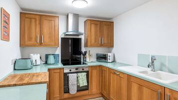 A compact kitchen with wooden cabinets, a stove, a toaster, and a sink.