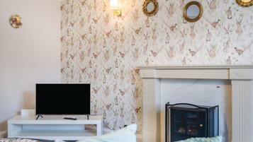 Sala de estar com televisão sobre suporte branco, lareira e papel de parede estampado.