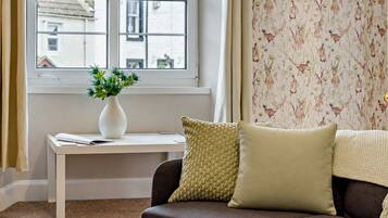 A room with a window, a white desk, a brown sofa, and a patterned wallpaper.
