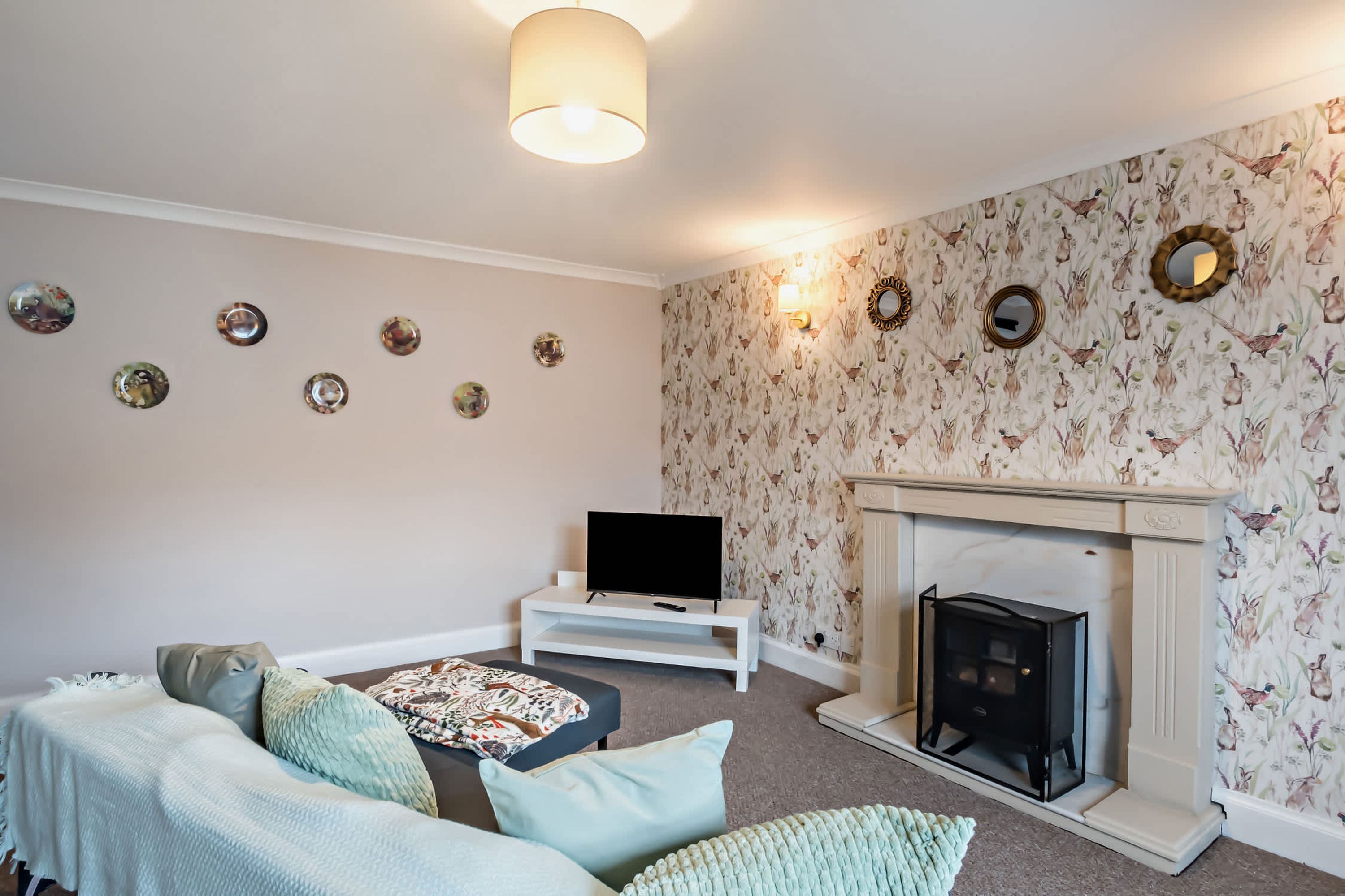 A living room with a sofa, a flat-screen TV, a fireplace, and decorative wall sconces.