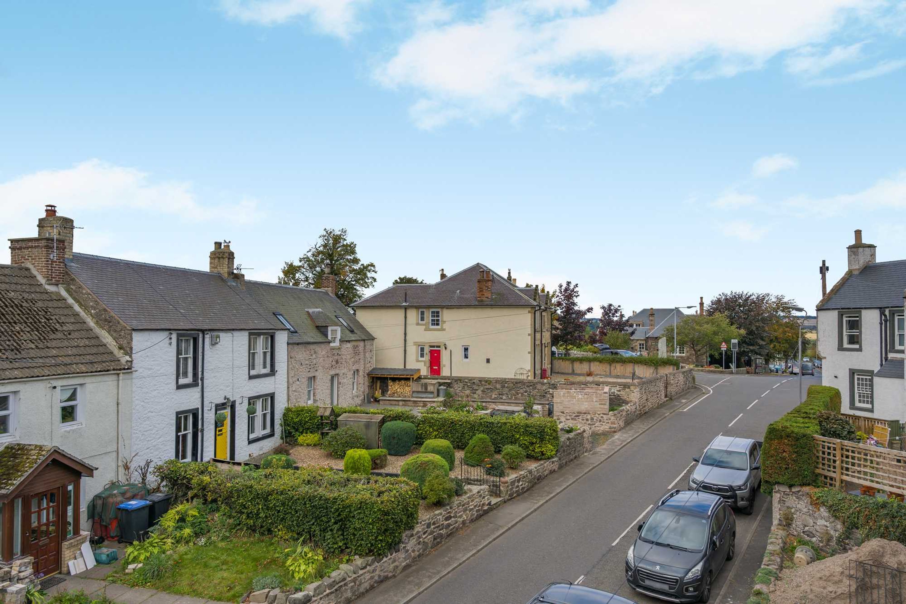 A residential street with houses, parked cars, and a clear sky.
