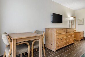 Une pièce avec une table et des chaises en bois, une commode en bois, un téléviseur à écran plat fixé au mur et un lampadaire.