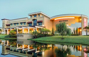 Ein großes, modernes Gebäude mit einer geschwungenen Fassade, einem zentralen Eingang und einem Spiegelbild in einem Wasserspiel.