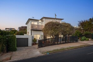 Ein modernes, zweigeschossiges Haus mit Garage, umzäunter Garten und Blick auf die Straße.