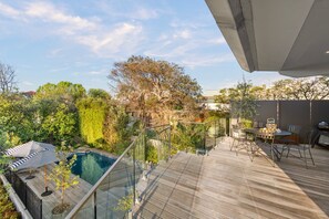 Eine Dachterrasse mit Pool, Gartenmöbeln und Glasgeländer.