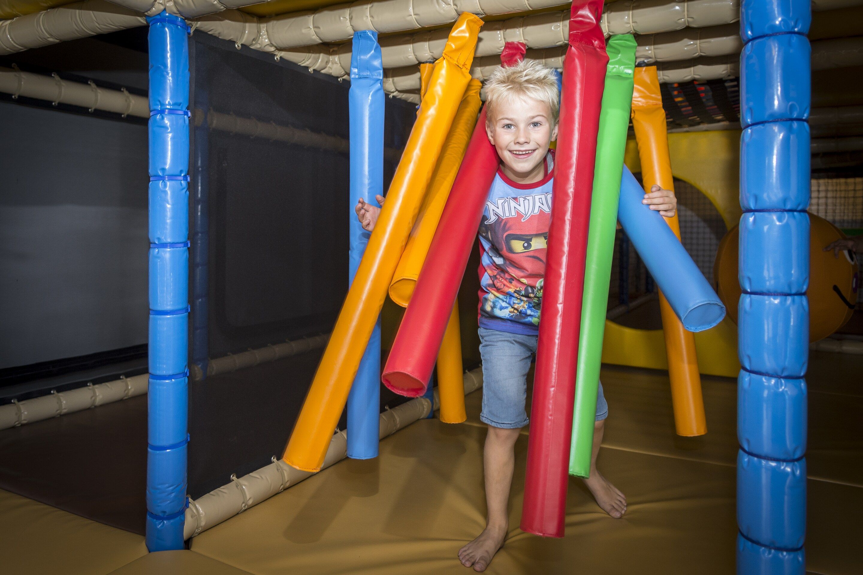 A child playing on a multi-colored play structure with various tubes and poles.