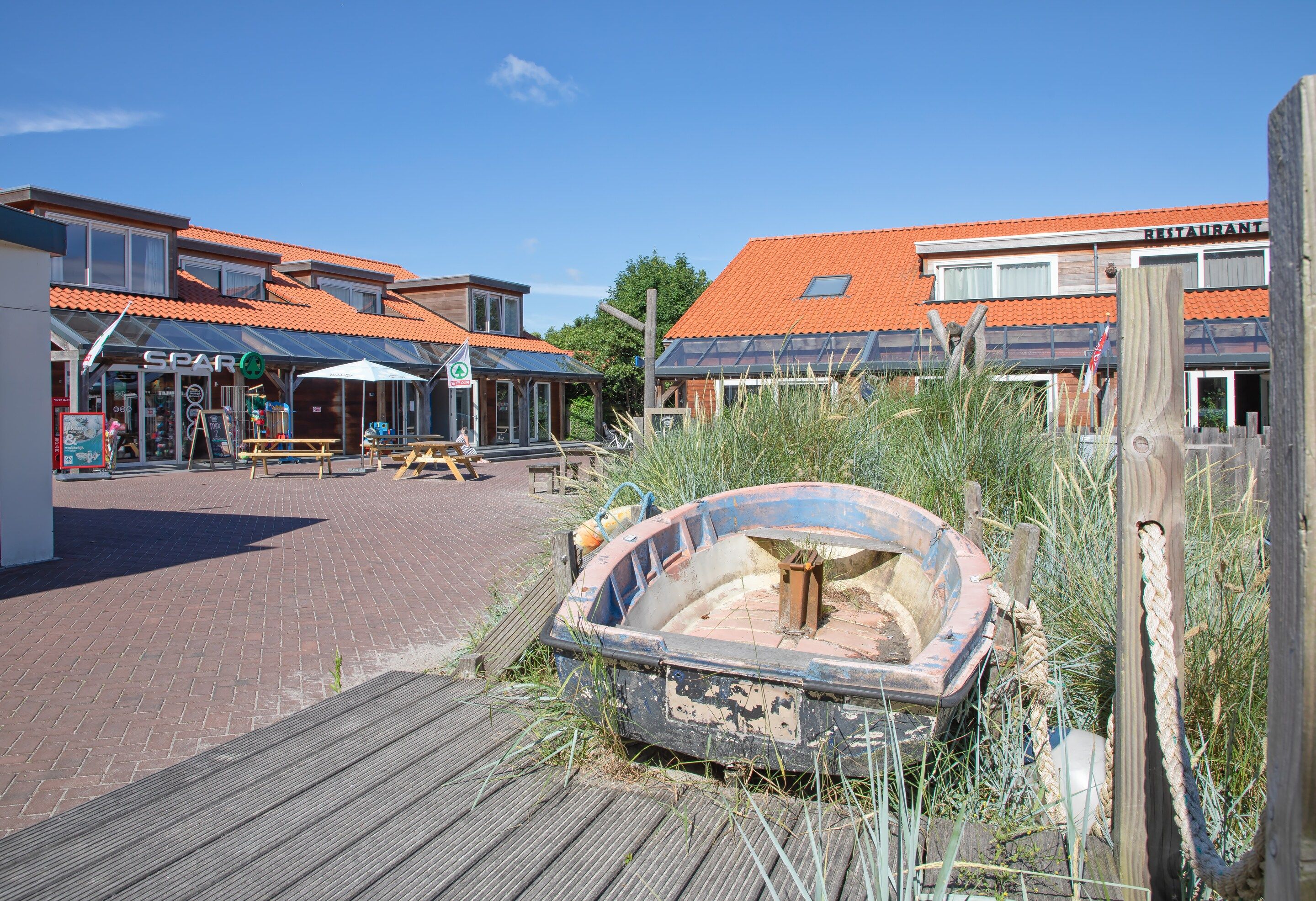 Een pand aan het water met een boot, een houten terras en gebouwen met rode pannendaken.