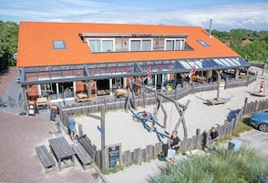 Um restaurante com telhado de telhas vermelhas, área de estar ao ar livre e cerca de madeira.