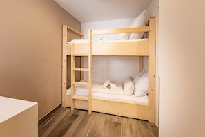 Un llit superposat amb una escala, roba de llit blanca i un sòl de fusta.