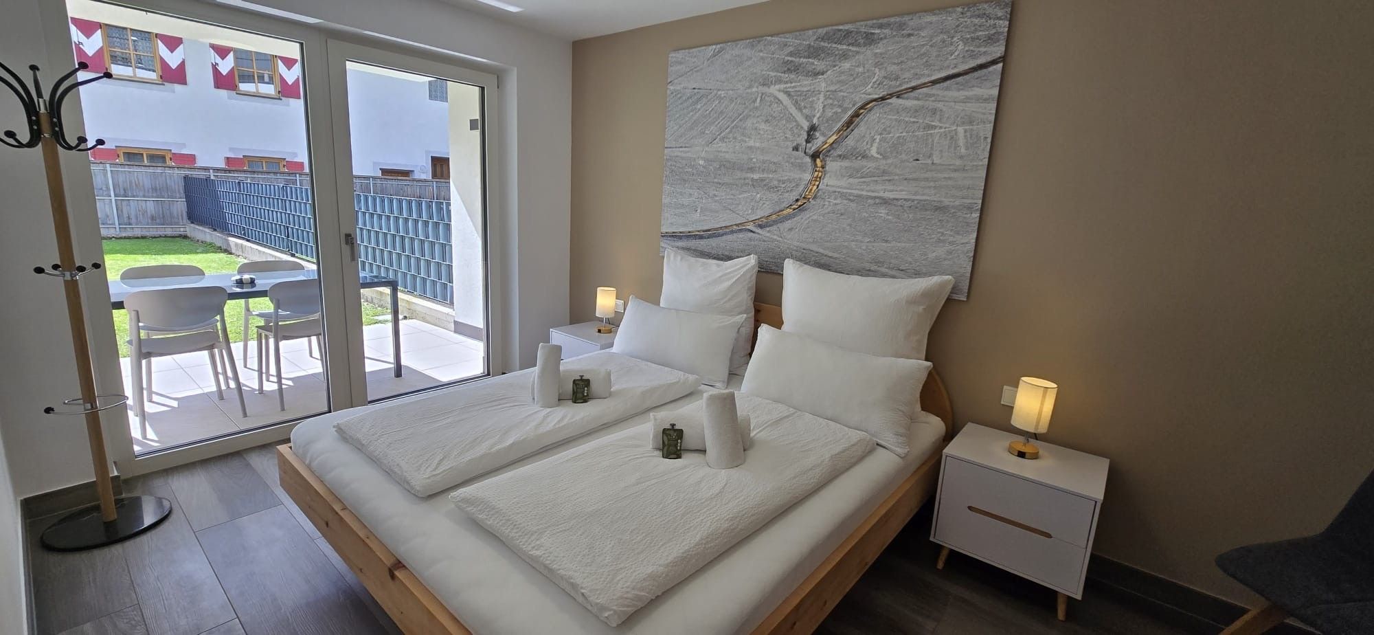 Ein Hotelzimmer mit einem großen Bett, Nachttischen, Blick ins Freie und einem modernen abstrakten Gemälde an der Wand.