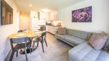 Ein modernes Wohnzimmer mit einem grauen Sofa, einem Esstisch für vier Personen und einer Küche im Hintergrund.