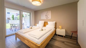 Ein modernes Schlafzimmer mit einem hölzernen Bett, einem Nachttisch, einem Sessel und Blick ins Freie.
