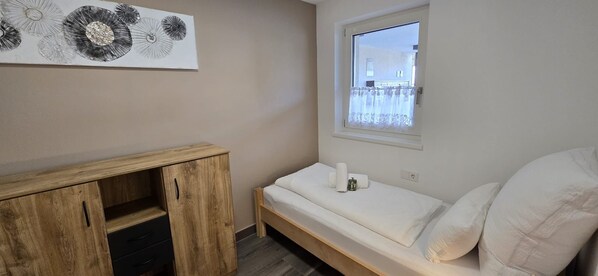 Una stanza piccola e pulita con un letto, un armadietto in legno e una finestra vista.