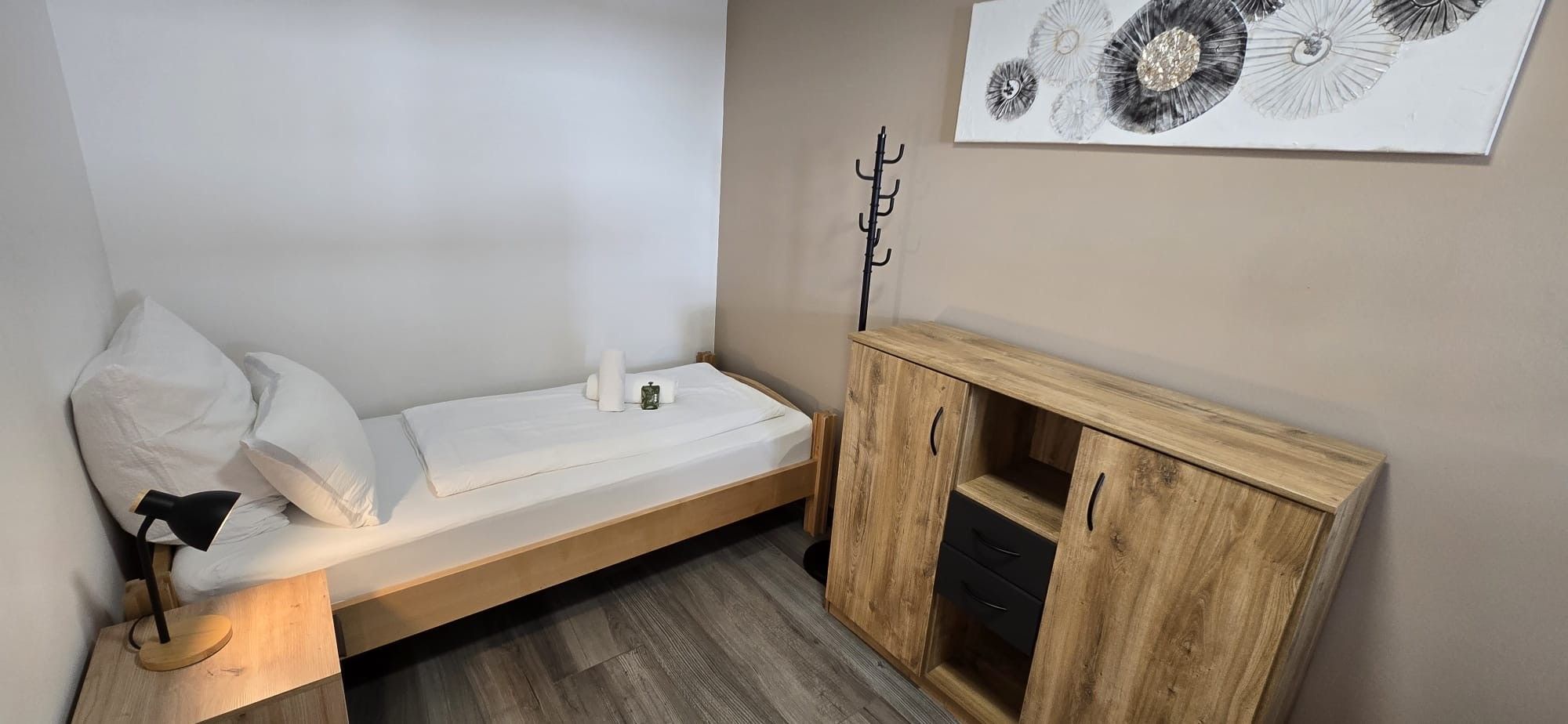 Ein kleines Zimmer mit einem Einzelbett, einem Holzschrank und einem Wandhaken für Kleidung.
