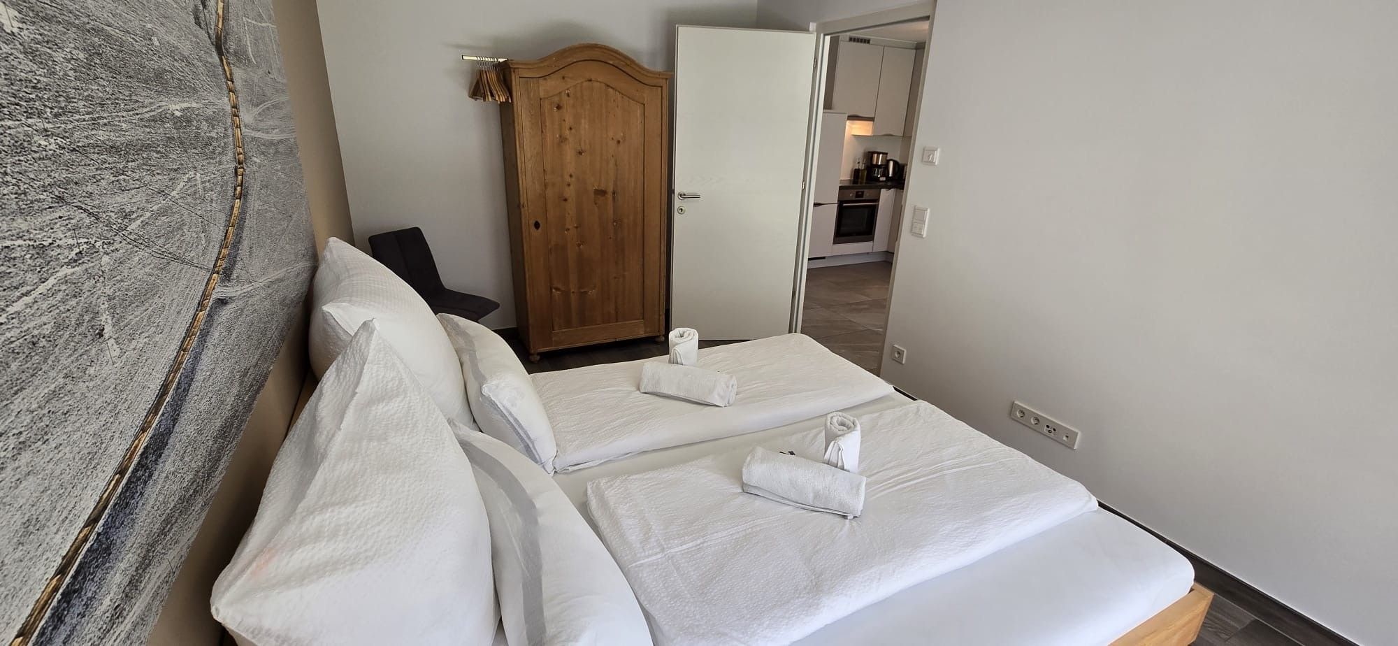 Une chambre d’hôtel avec un lit, une armoire en bois et, au fond, une petite cuisine.