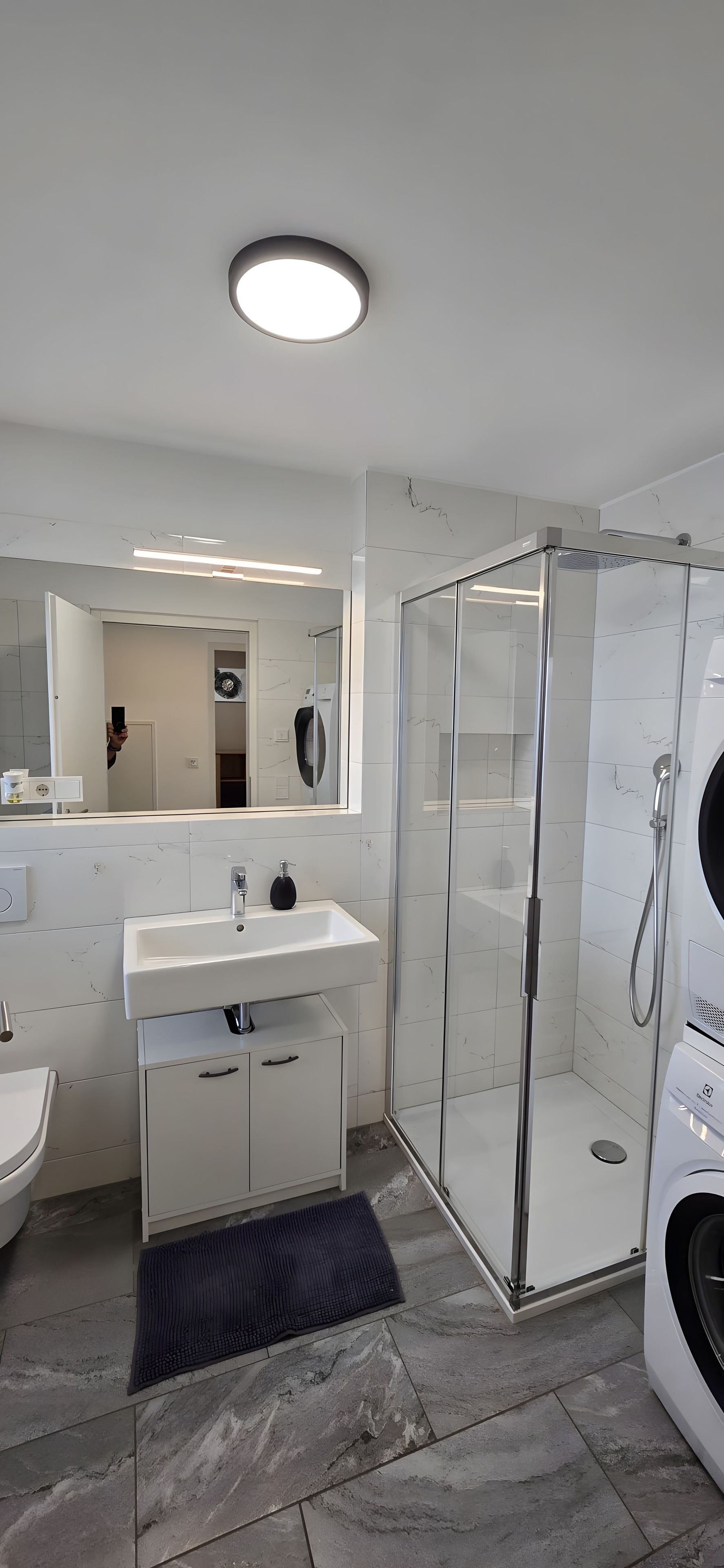 Un bagno moderno con cabina doccia in vetro, lavandino bianco e uno specchio grande.