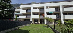 Un edificio residenziale a più piani con balconi, un piccolo prato e un ingresso chiuso da cancello.