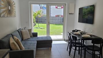 Ein modernes Wohnzimmer mit einem grauen Ecksofa, einem Esstisch für vier Personen und einer Schiebetür zu einem Garten.