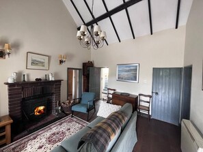 A living room with a fireplace, a sofa, a blue armchair, and a wooden door. - Cosy Fisherman’s Cottage by the Beach & Lighthouse (Llaneilian)