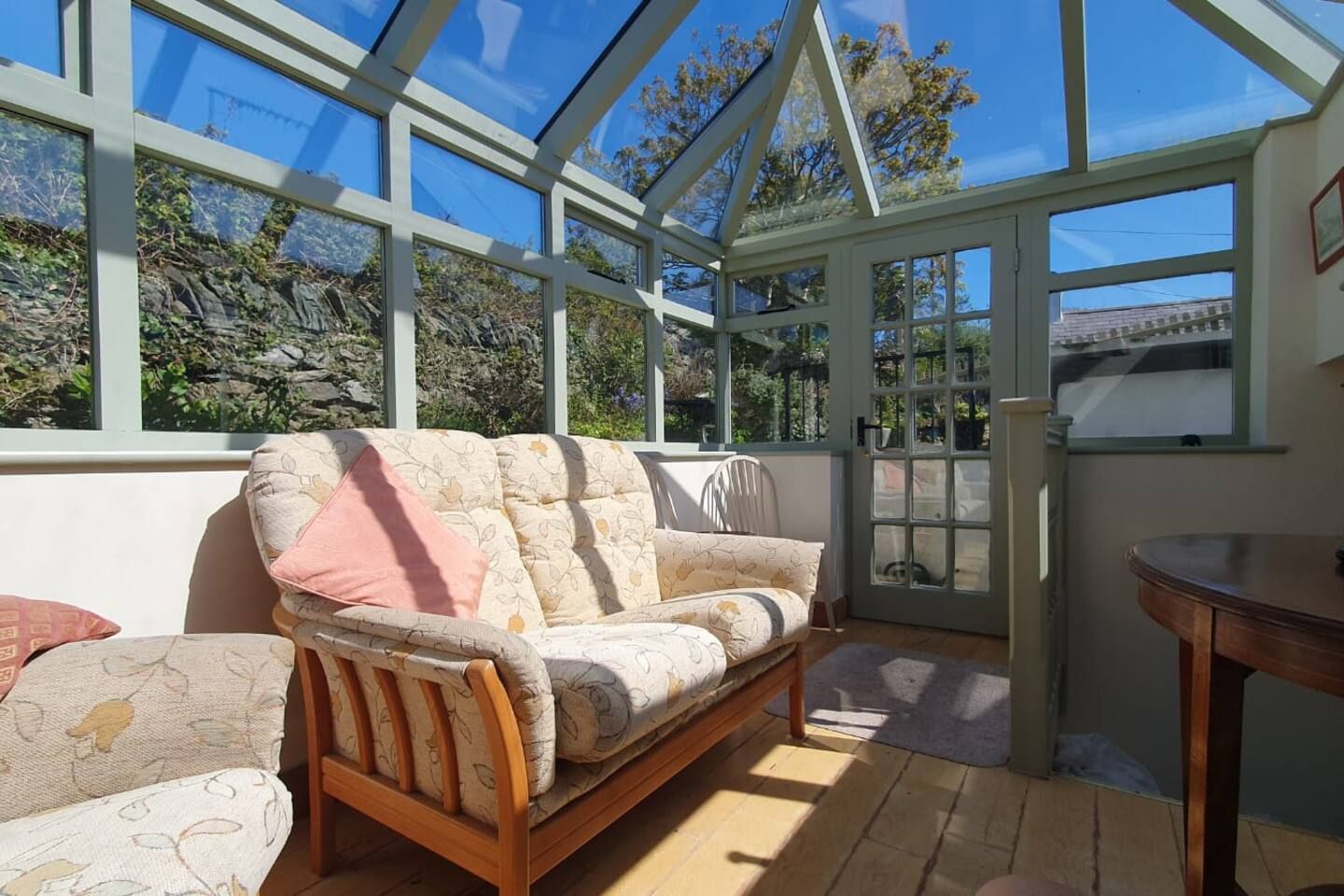 A conservatory with a wooden sofa, a table, and a view of the outdoors.