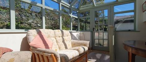 A conservatory with a wooden sofa, a table, and a view of the outdoors.