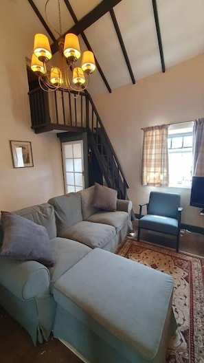 Uma sala de estar com sofá de canto, uma poltrona, escada e lustre.