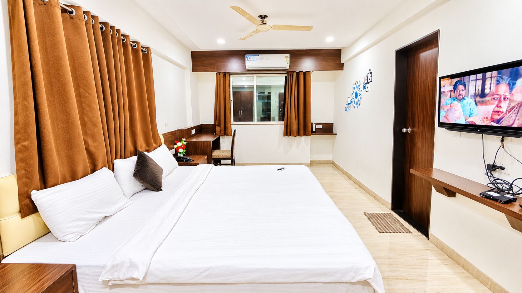 Une chambre d’hôtel équipée d’un lit, d’un bureau, d’une chaise, d’une télévision et d’un ventilateur de plafond.