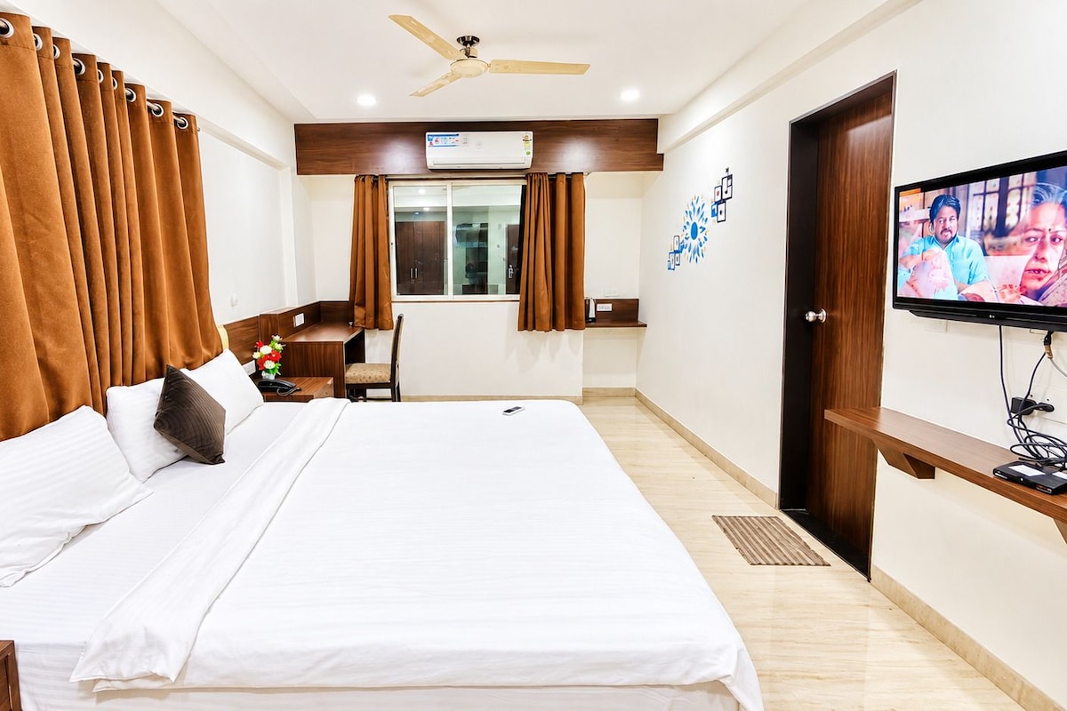 A hotel room with a bed, a desk, a chair, a television, and a ceiling fan.