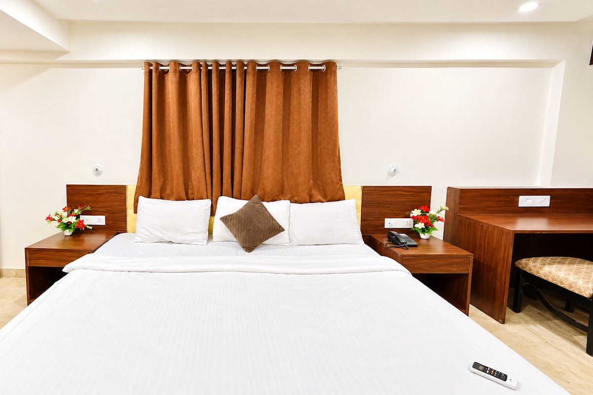 A hotel room with a large bed, wooden headboard, two bedside tables with lamps, a desk, and a chair.