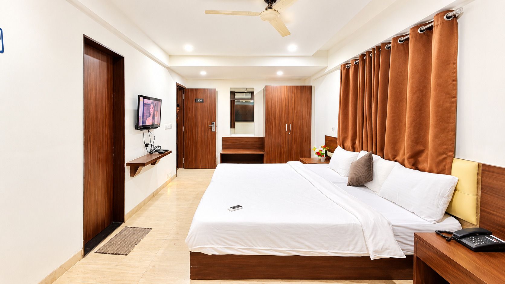 A hotel room with a bed, bedside table, and a television on the wall.