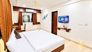 Habitación de hotel con cama, televisión, escritorio y ventana con cortinas.