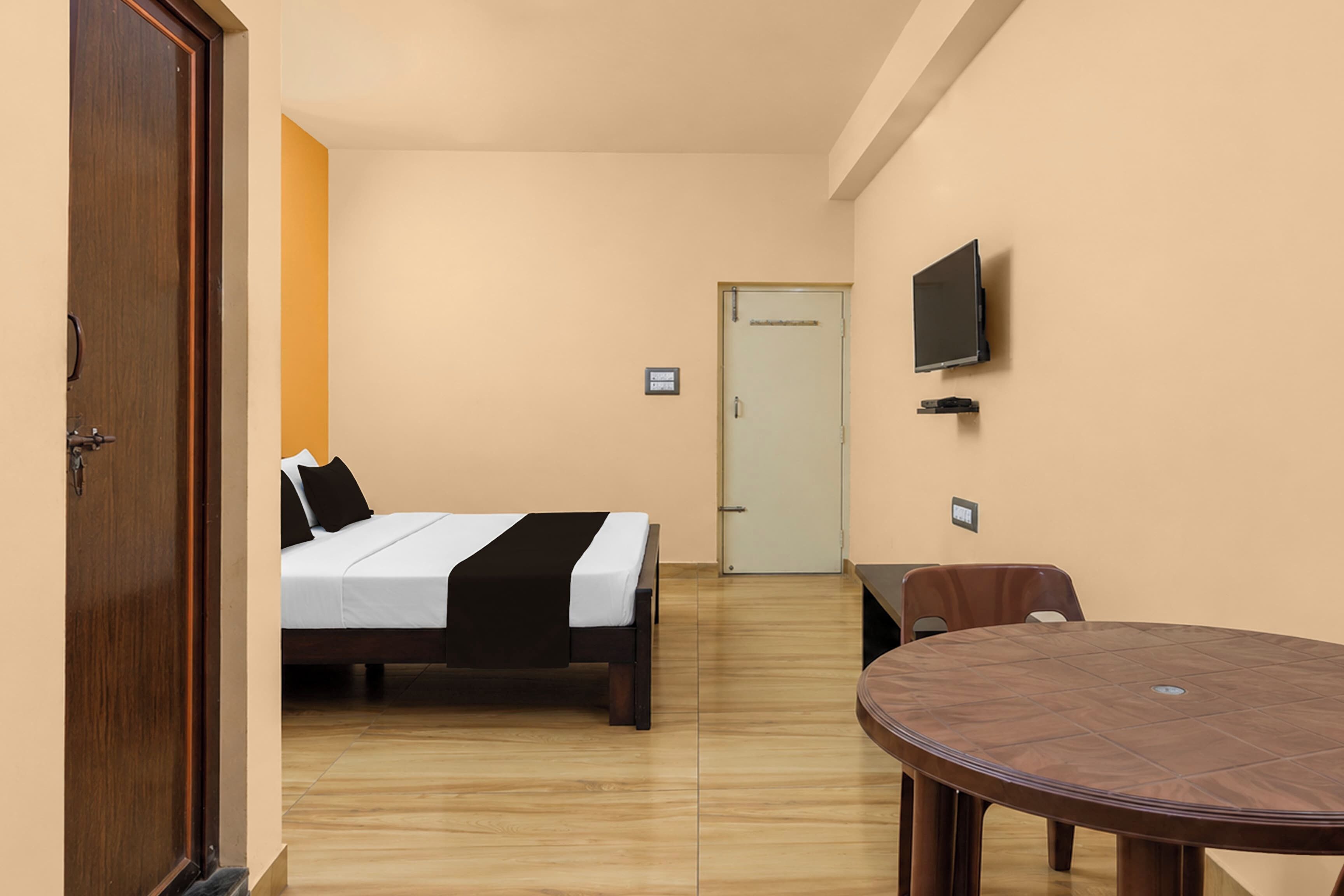 A hotel room with a bed, a desk, a chair, a television, and a door.