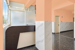 Corredor de hotel com balcão de recepção, uma porta e uma janela com persianas.