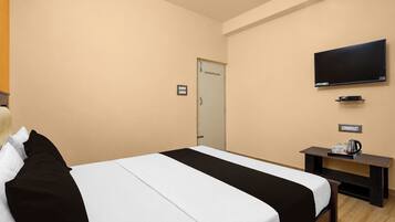 A hotel room with a bed, a television mounted on the wall, a small table with a kettle and cup, and a door.