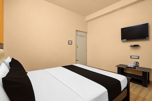 Quarto de hotel com cama, televisão na parede, uma mesinha com chaleira e chávena, e uma porta.