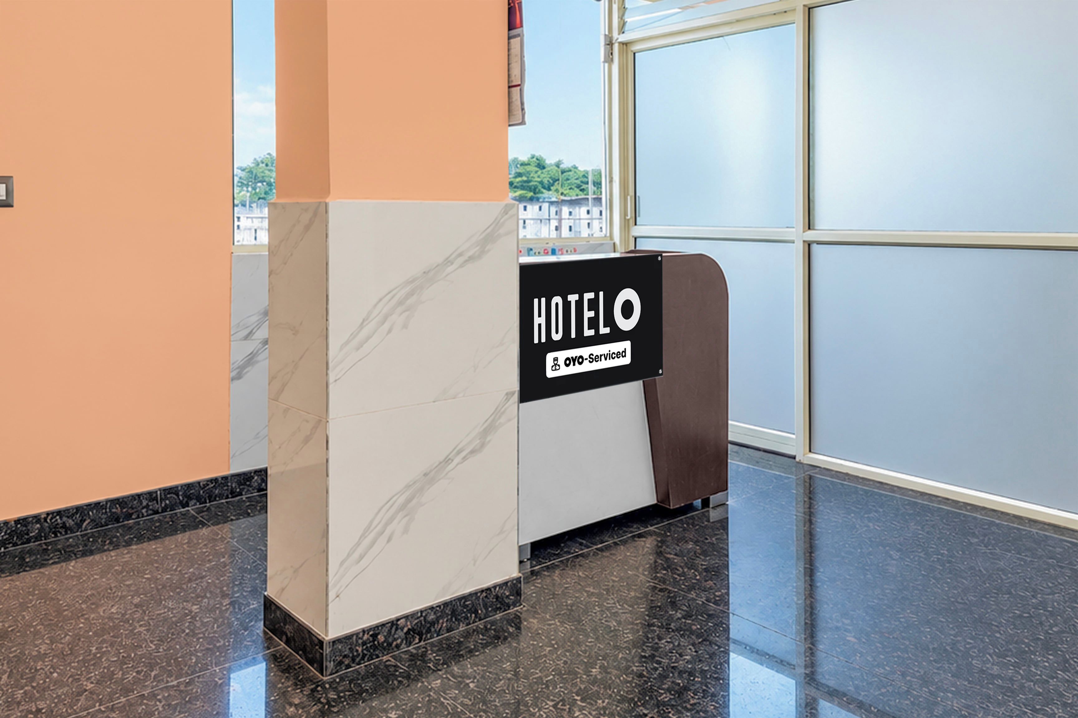 A hotel reception desk with a marble column, a black sign indicating it is fully serviced, and a view of the outside through large windows.
