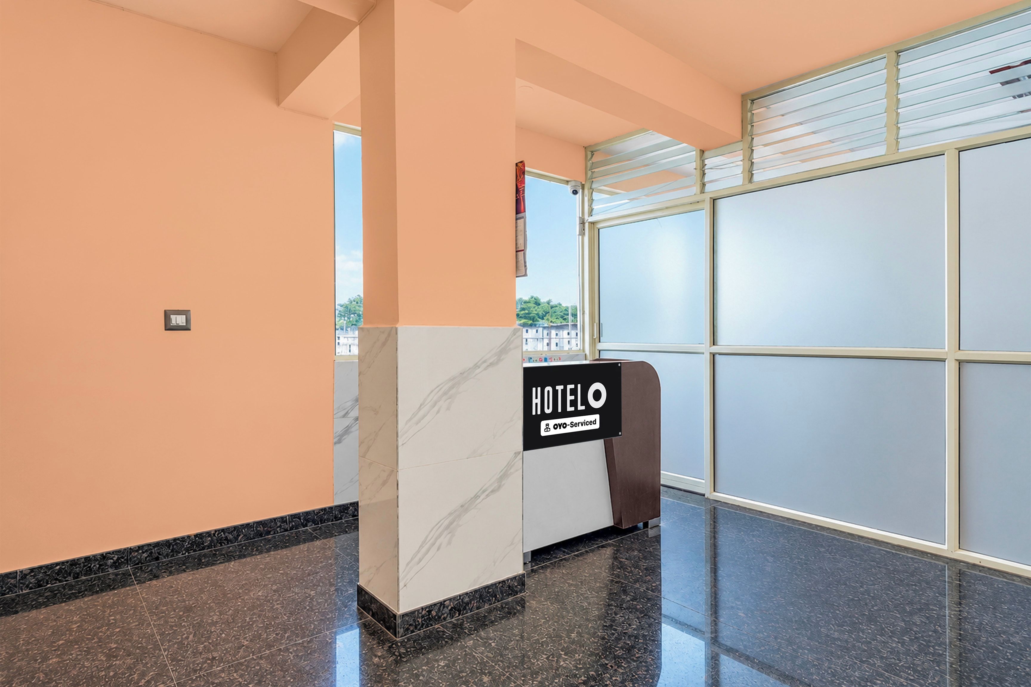 A hotel reception area with a marble counter, a sign indicating it is serviced by OYO, and a large window with blinds.