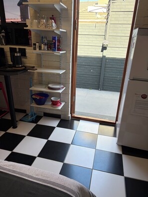 Una cucina con pavimento a scacchi bianconero, un frigorifero ed scaffali con diversi utensili da cucina.