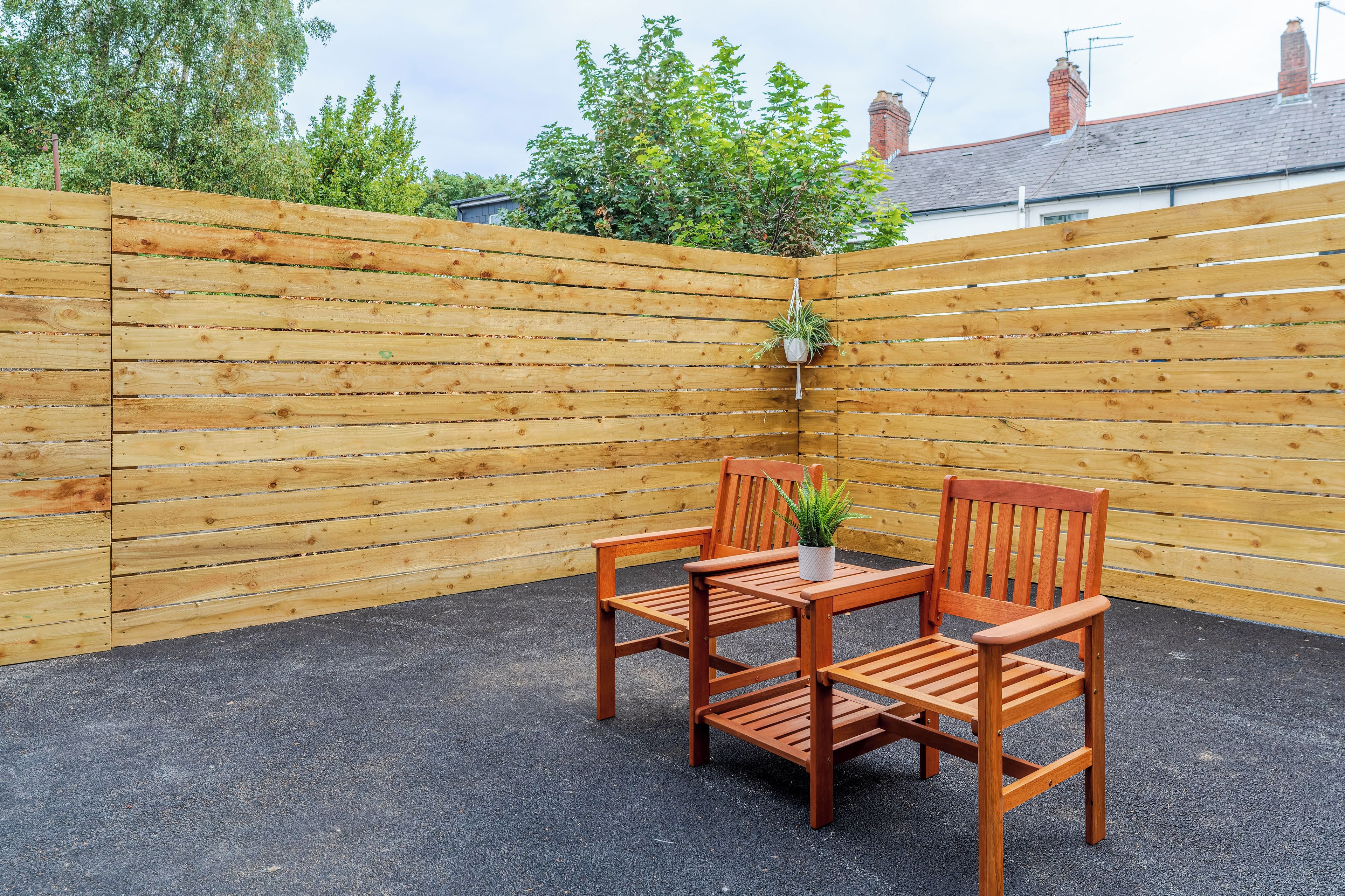 A wooden patio with a table and two chairs, a potted plant, and a wooden fence.
