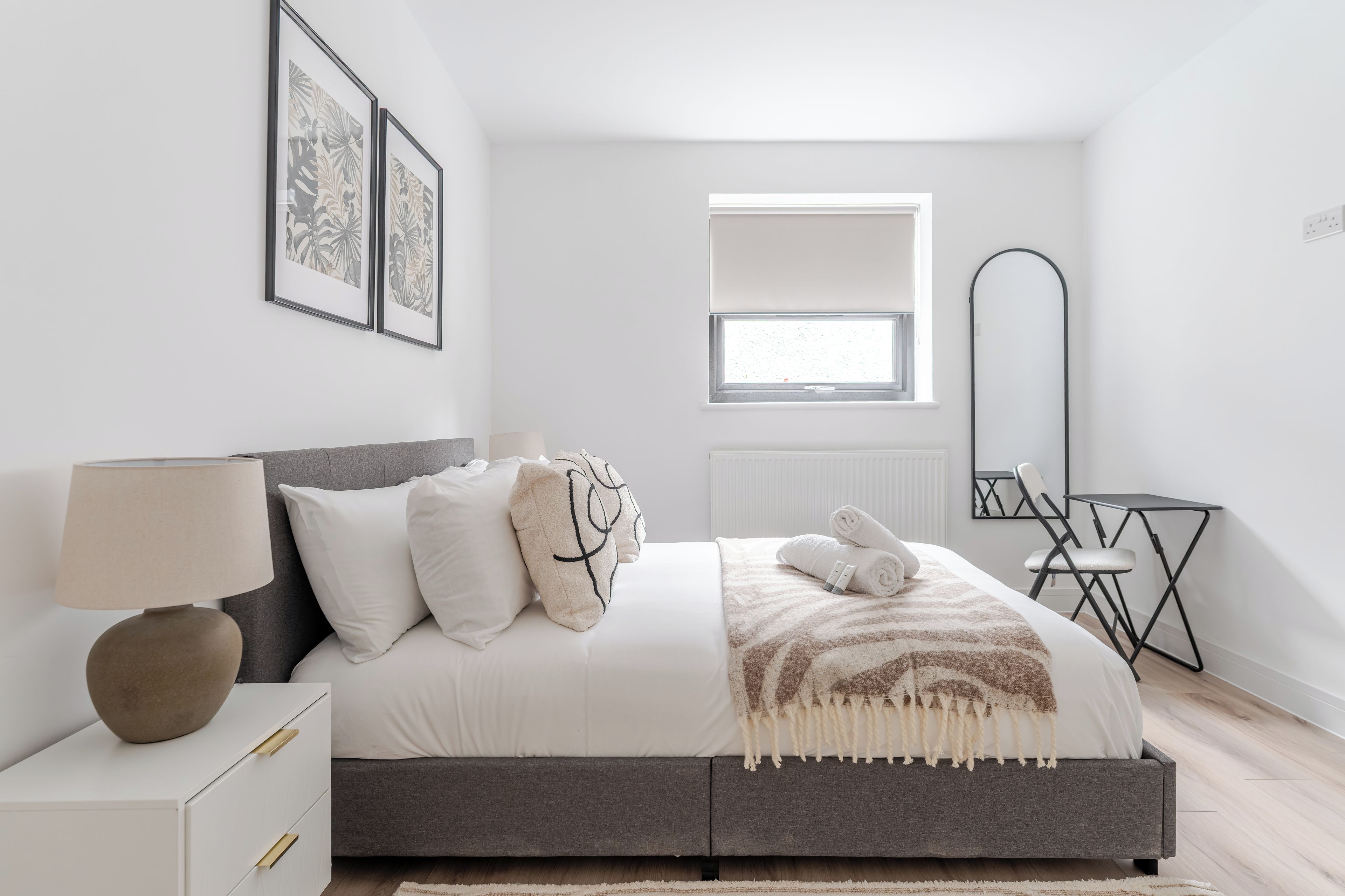 Un dormitorio moderno con cama, mesita de noche, lámpara y ventana.