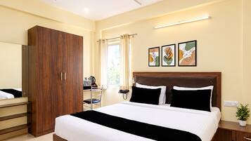 Habitación de hotel con una cama grande, un armario, un escritorio con silla y una ventana con cortinas. Hay tres obras de arte enmarcadas en la pared.