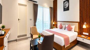 A hotel room with a bed, bedside tables, a desk, a chair, an air conditioning unit, and a window with curtains.
